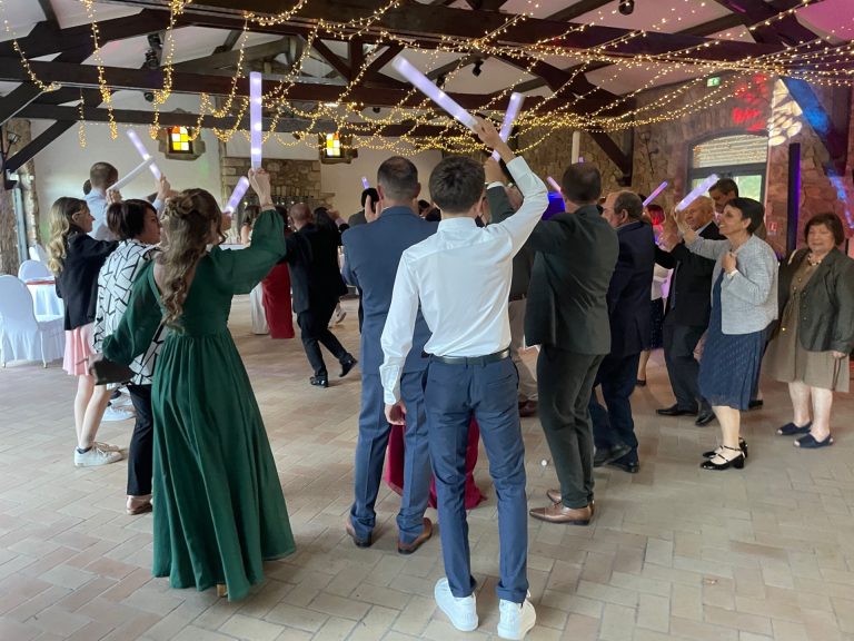Invités dansant avec des bâtons lumineux sous une charpente décorée de guirlandes