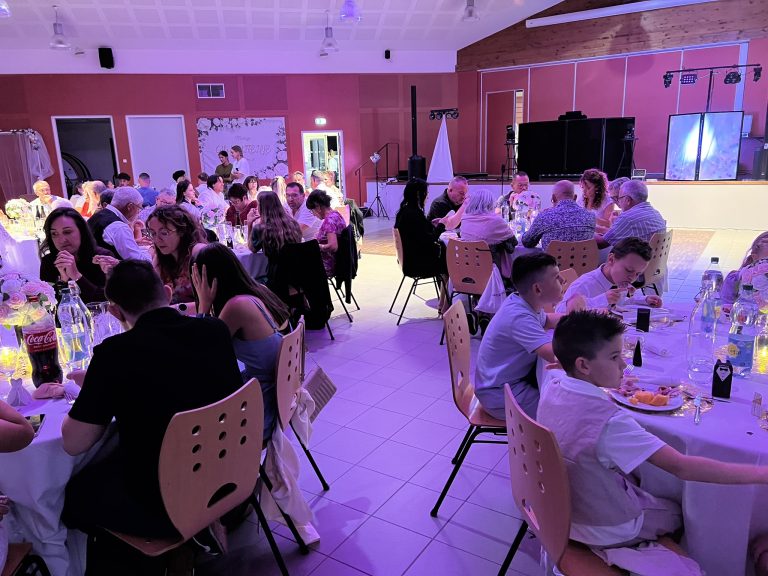 Convives attablés dans une salle des fêtes éclairée en violet pendant un repas animé