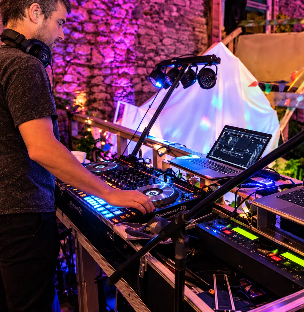 DJ aux platines avec contrôleur et ordinateur, sous des lumières violettes